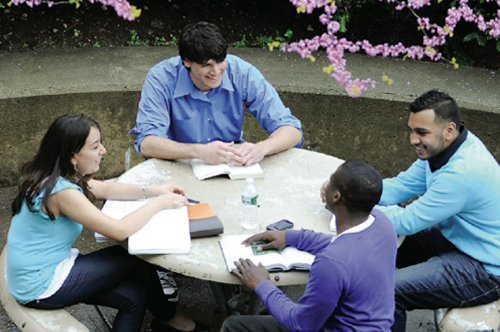 Students sitting at table outside talkignand smiling with their books and study materils on the table spread out. 