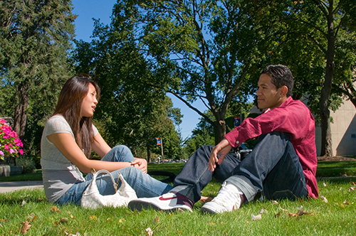 Two students taling, sittignon grass in front of a gazebo.