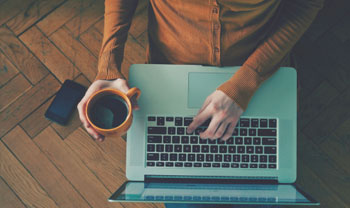 person sitting with laptop on lap with cup of coffee inhand