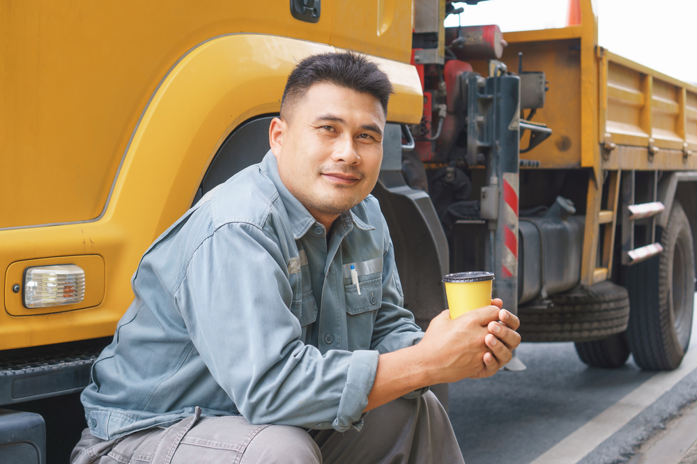 truck driver sittign in front of truck with a cup of coffee in his hand
